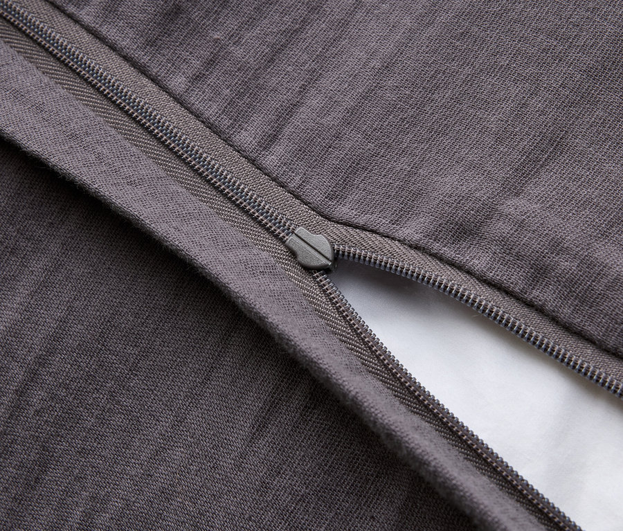 Egy részben nyitott, szürke párnahuzat közeli képe, cipzárral, amely egy fehér betétet tár fel.