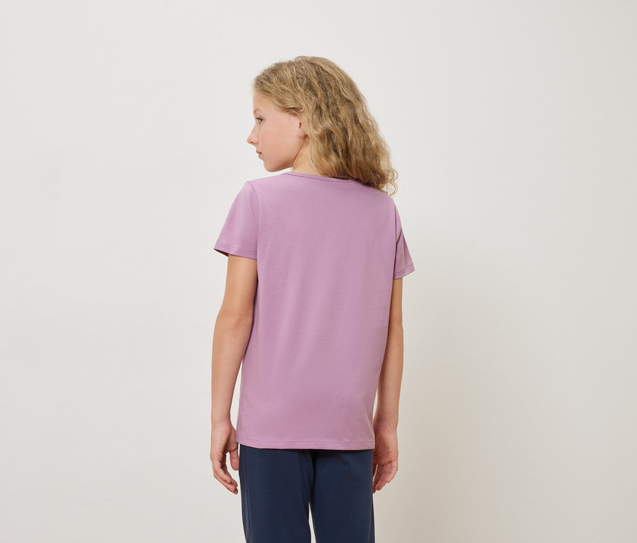 Hátulnézet egy szőke lányról lila pólóban és kék nadrágban, fehér háttér előtt.