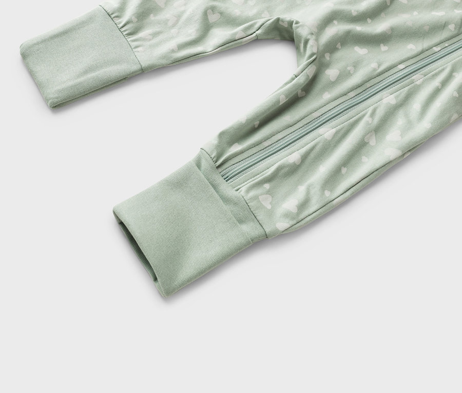 Egy világoszöld, fehér szívmintás, teljes hosszában cipzáras babapizsama közelképe.