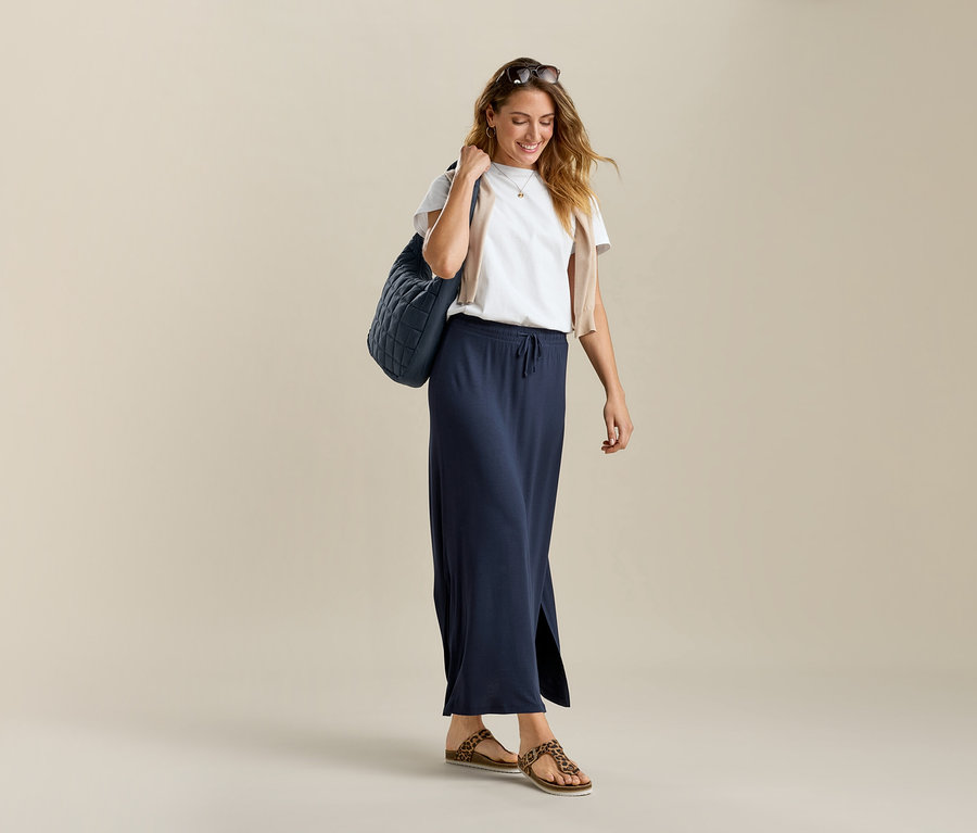 Nő fehér Basic pólóban és hosszú Langer Jerseyrock szoknyában. Táskát visz a vállán.