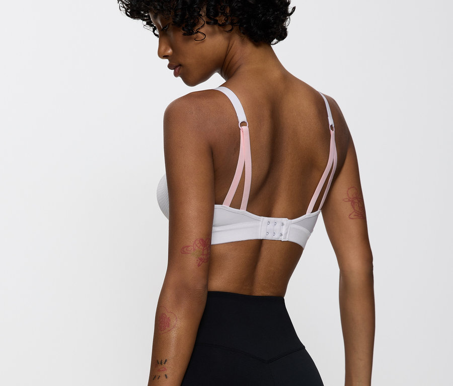 Nő visel egy fehér sportmelltartót rózsaszín pántokkal és fekete leggingset.