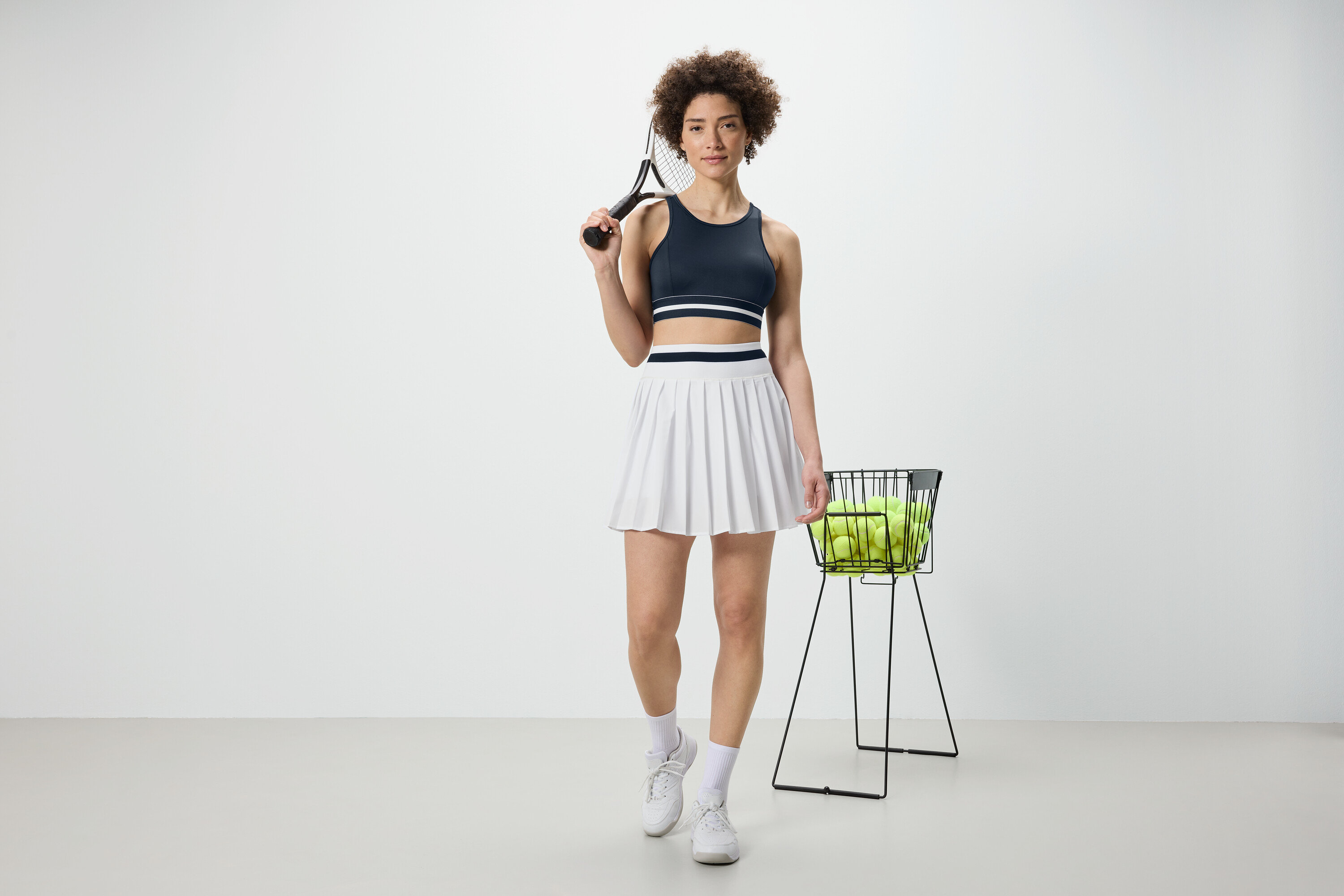 Nő teniszütőt tart és kék »Crop Top« sportmelltartót visel.
