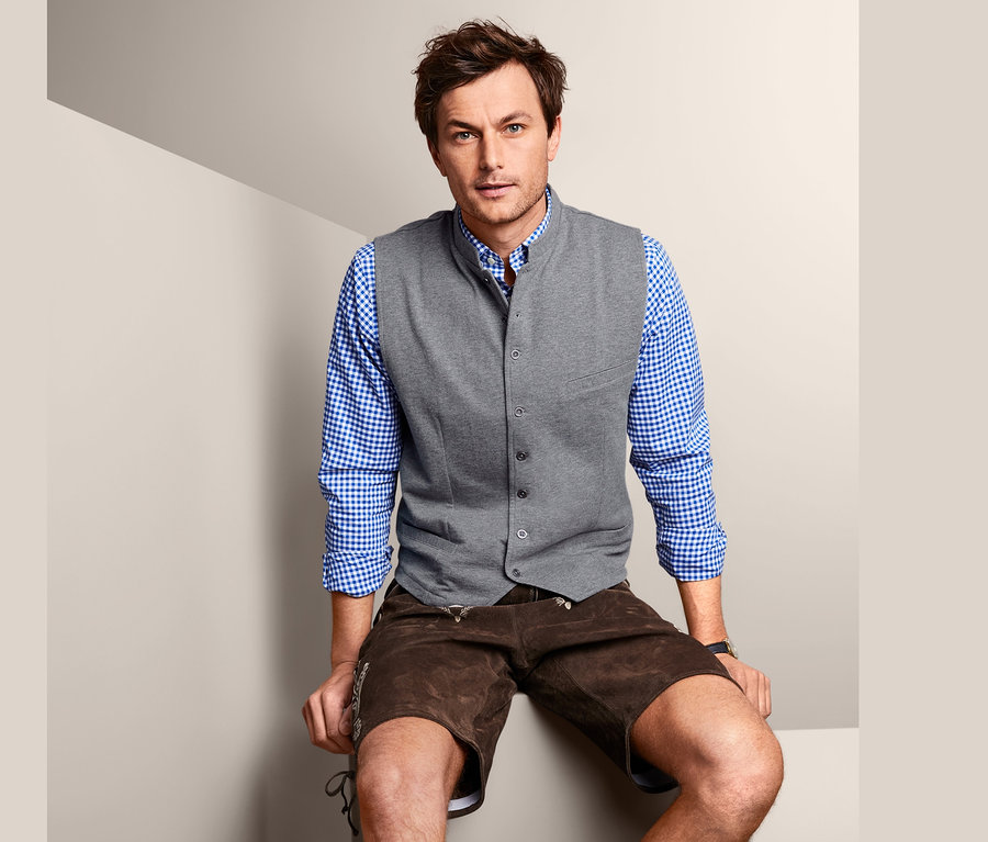 Férfi ül szürke férfi mellényben, ingben és rövid bőr nadrágban.