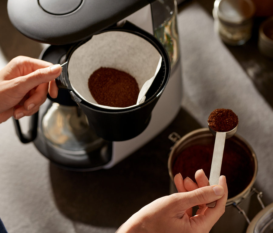 Nő kávét tesz egy fehér »Let's Brew« filteres kávéfőzőbe.