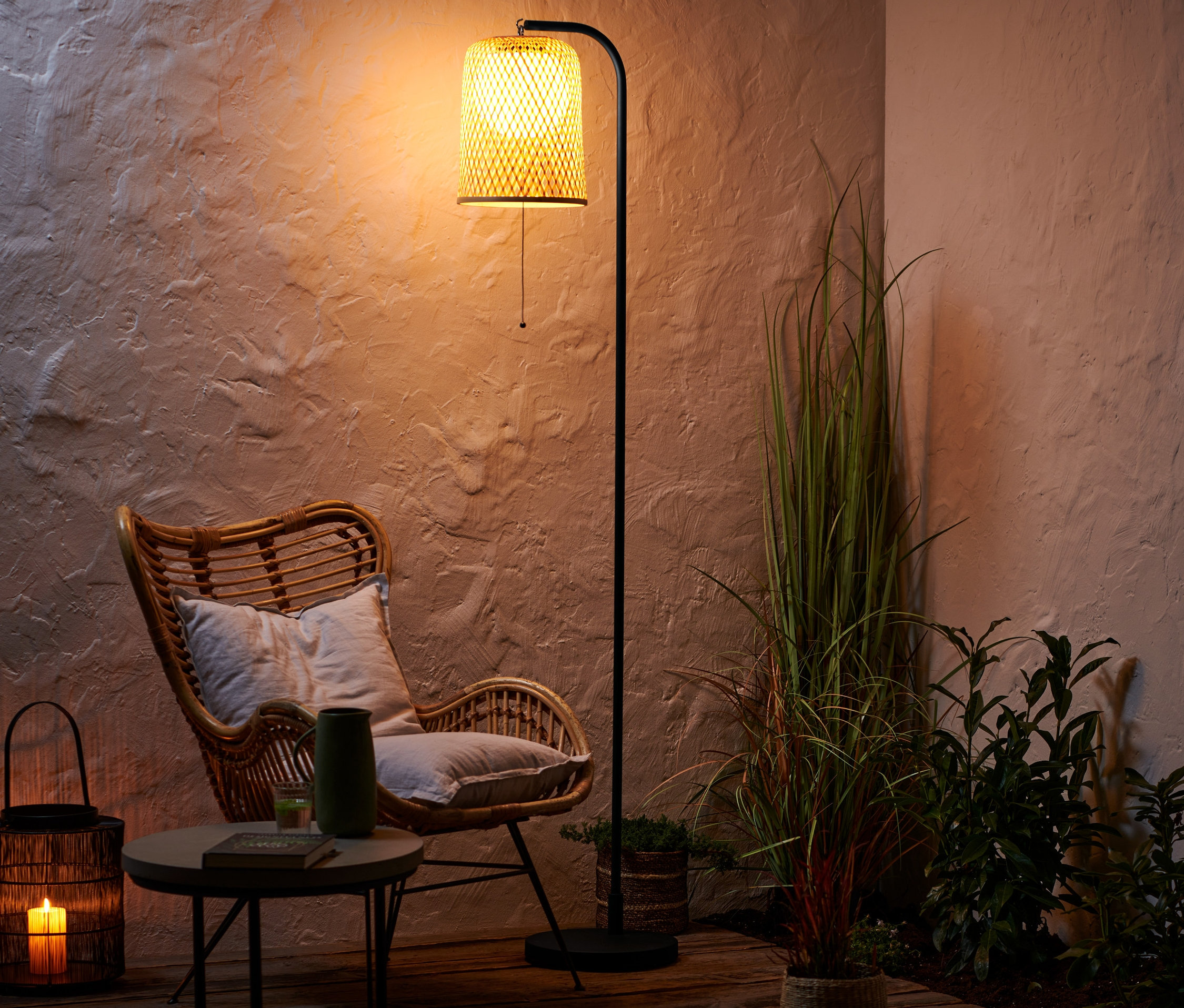 Egy rattan szék áll egy asztal mellett, rajta egy váza és egy könyv. Mögötte egy akkumulátoros állólámpa áll.