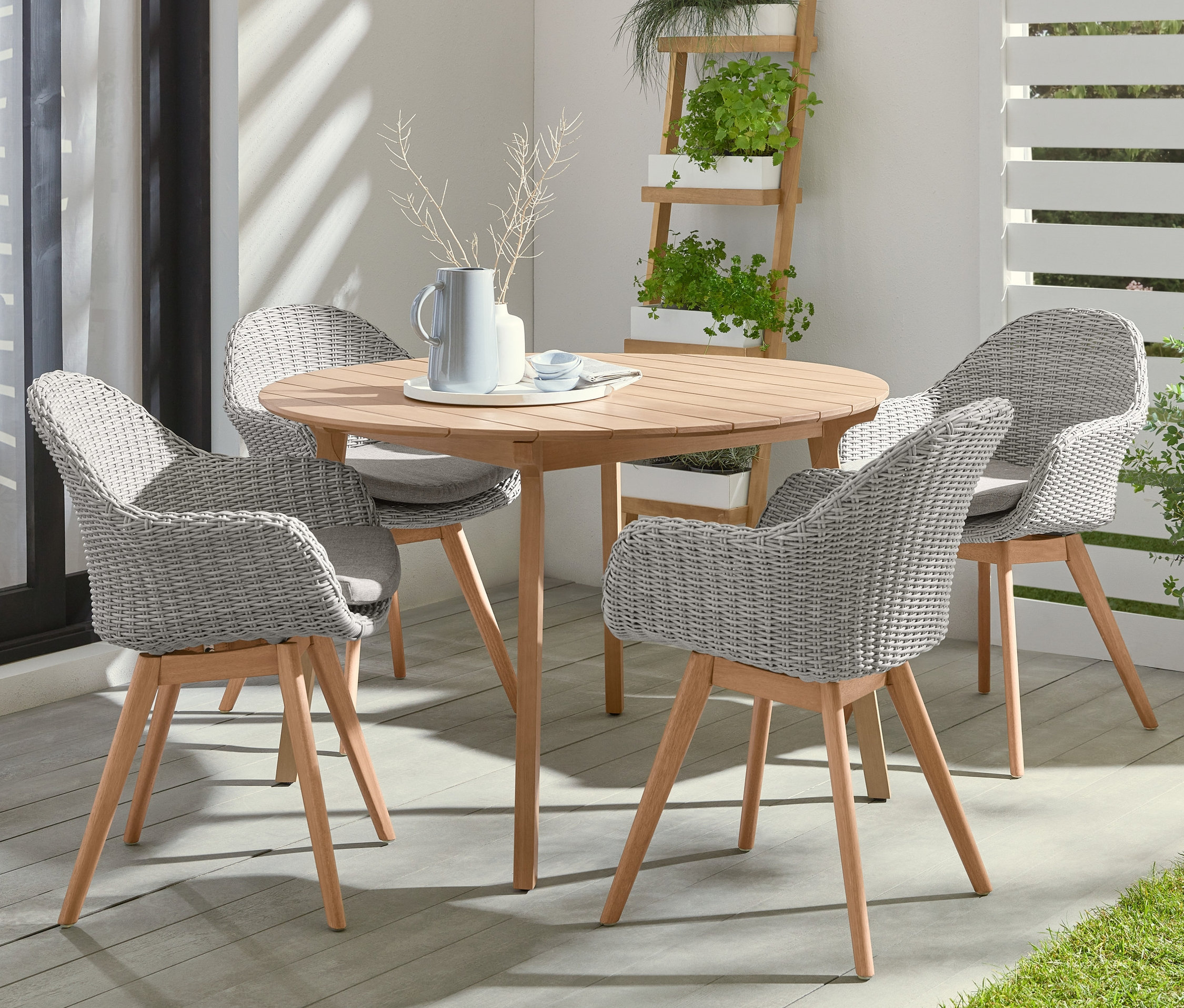 Négy szürke kerti kagylószék polyrattan fonattal vesz körül egy kerek asztalt. A háttérben kültéri LED-es állólámpa látható.