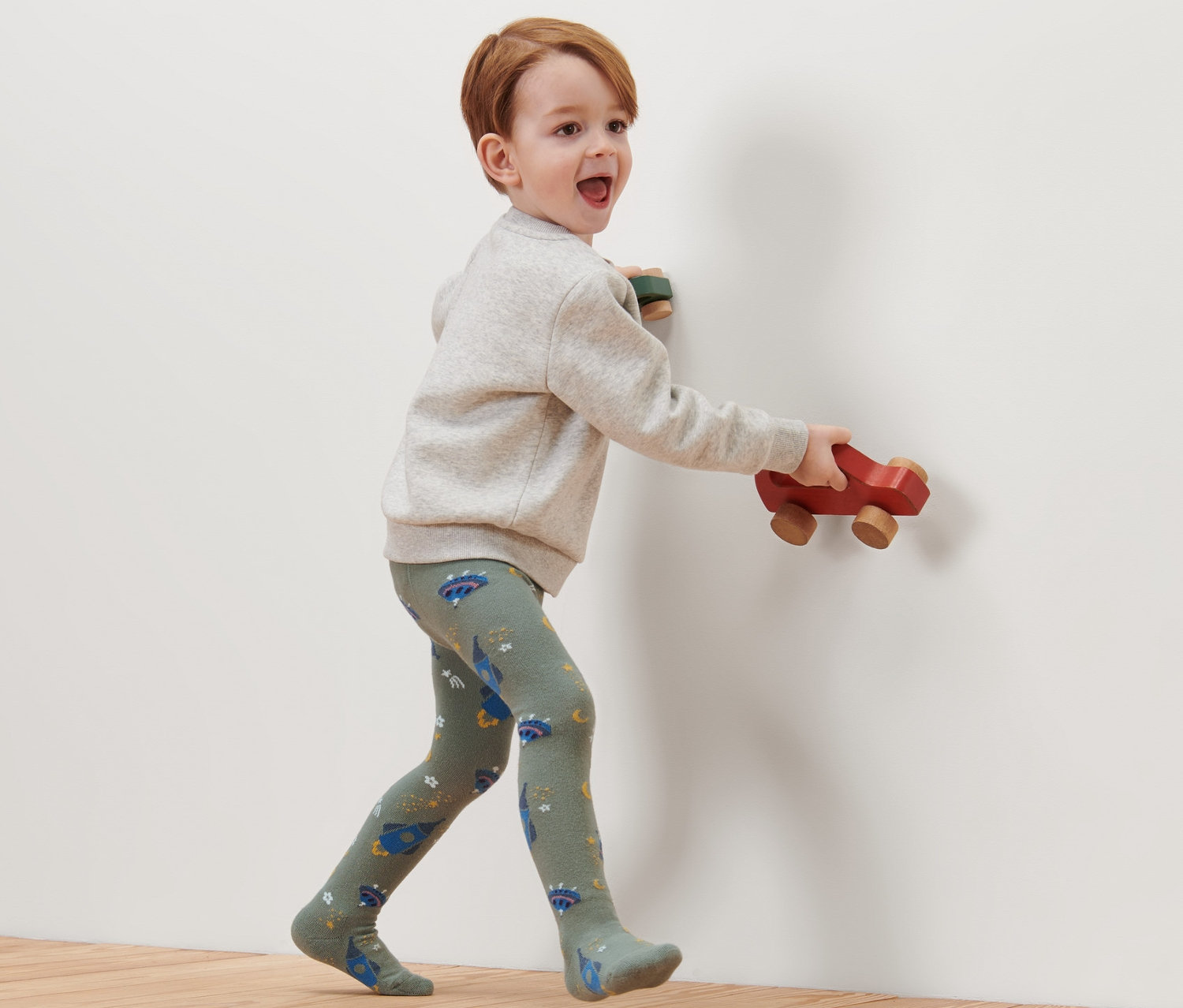 Egy fiú sétál a fapadlón, és világűr mintás pamut harisnyanadrágot visel.