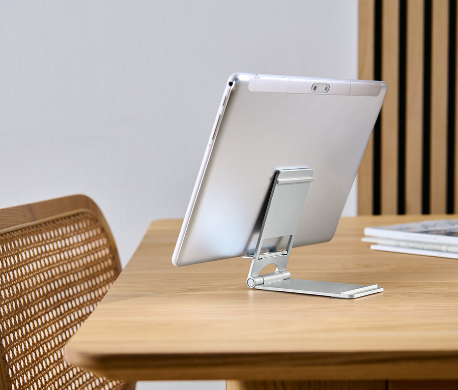 Tablet egy okostelefon- és táblagéptartón támaszkodik egy fa asztalon.