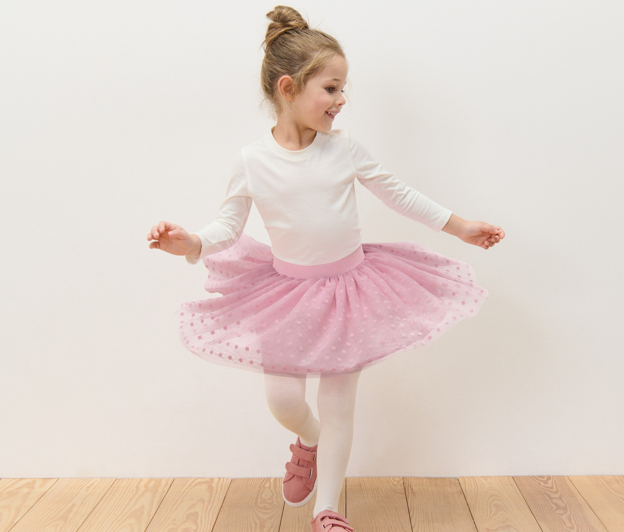 Kislány táncol fehér felsőben és rózsaszín virágos kislány tüllszoknyában.