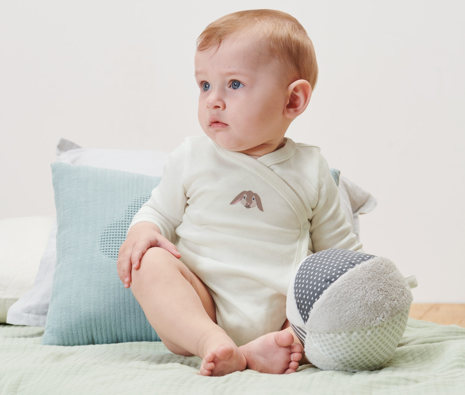 Egy baba ül az ágyon és 3 baba hosszú ujjú bodyt visel.