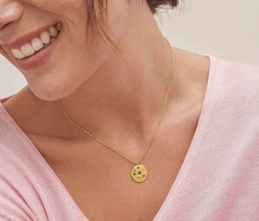 Egy mosolygó nő részlete, aki egy üvegköves medállal díszített nyakláncot és egy üvegkövekkel díszített fülbevalót visel.