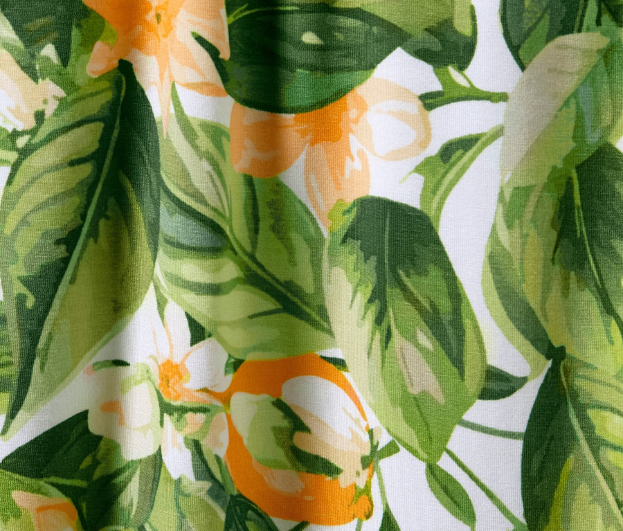 Közeli kép egy nyomott mintás palazzo nadrágról, zöld és narancssárga levelekkel és virágokkal, fehér alapon.
