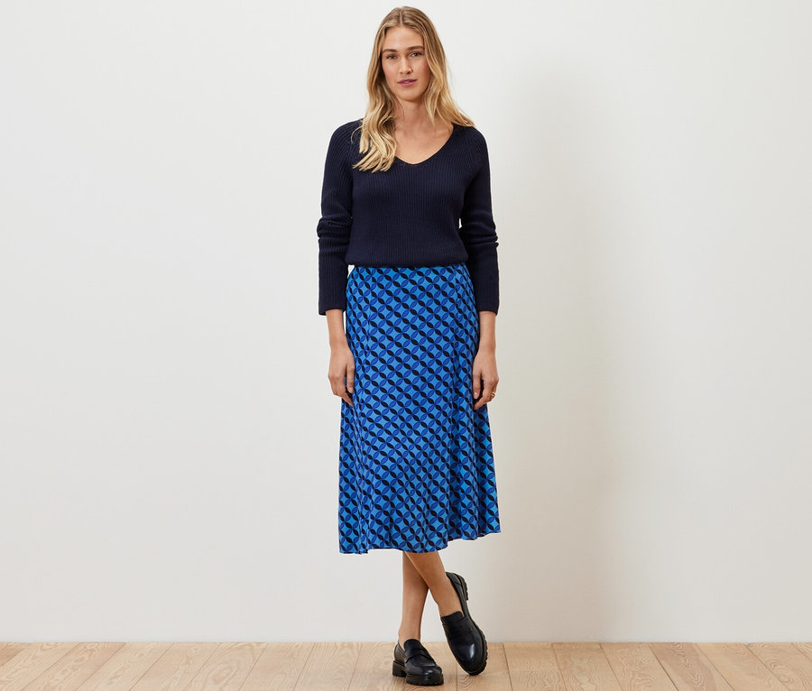 Nő pózol sötétkék pulóverben és mintás midi szoknyában.
