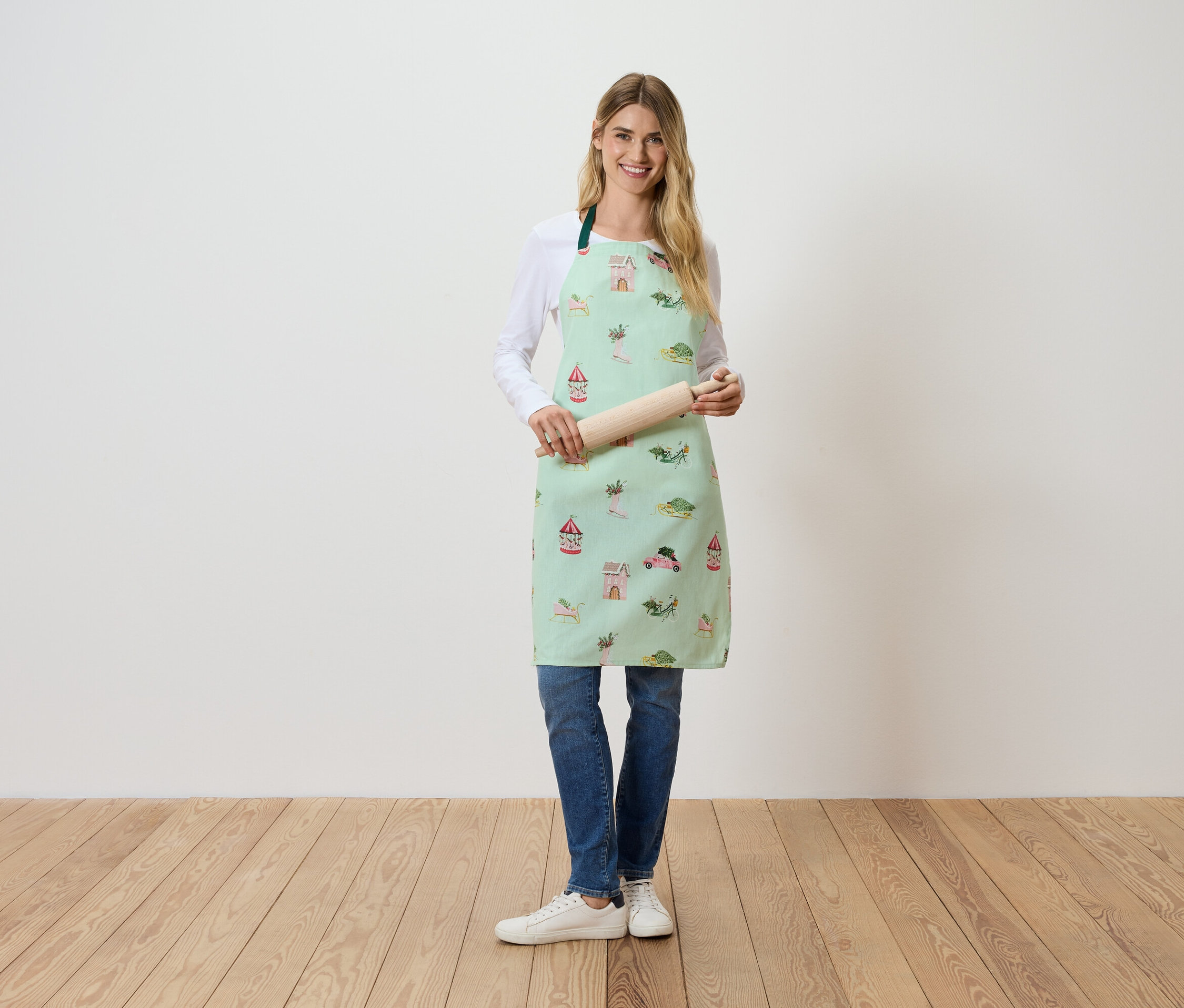 Egy nő áll és egy sodrófát tart. Világoszöld, mintás kötényt visel.