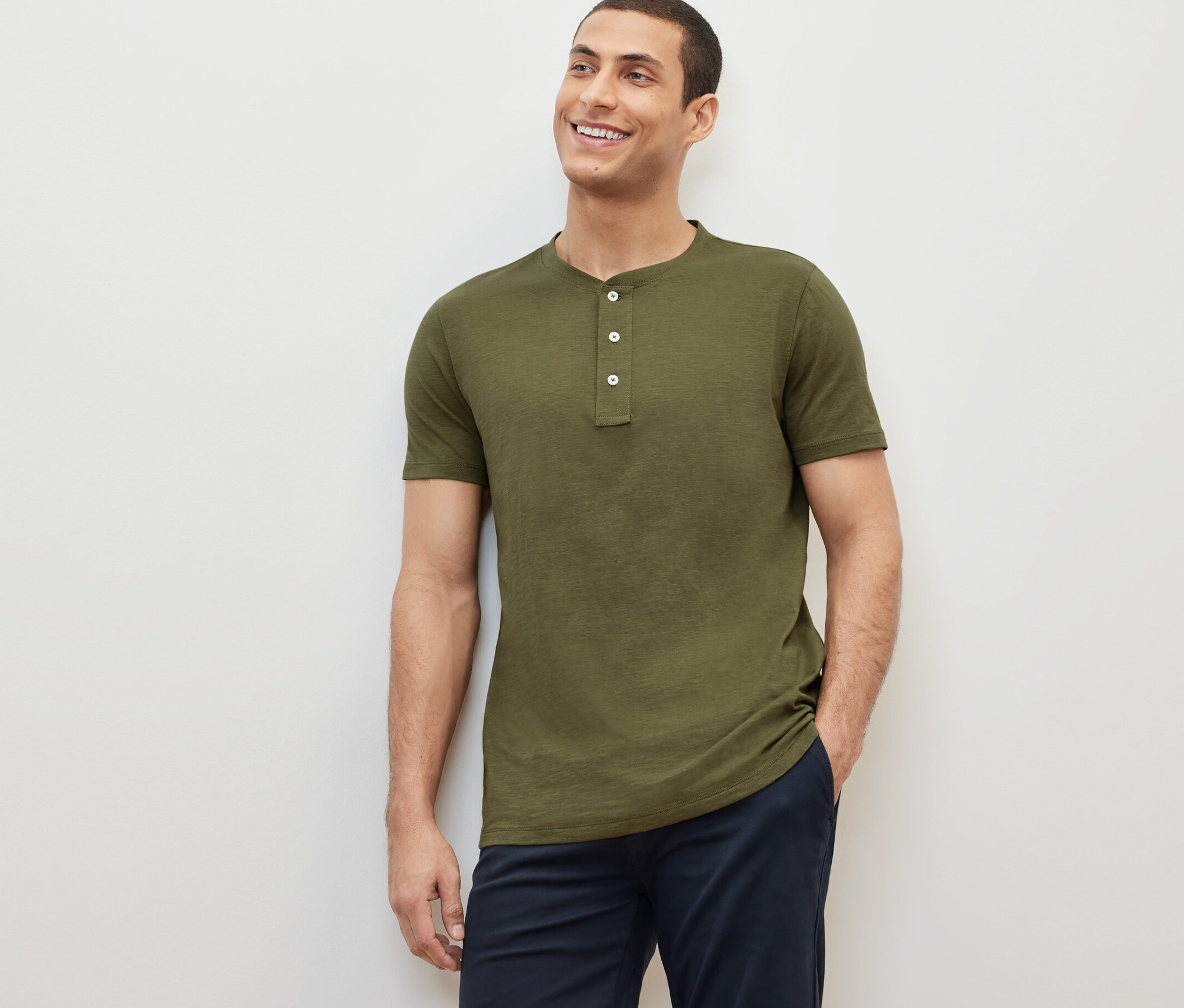 Mosolygó férfi pózol rövid ujjú, khaki színű henley felsőben.