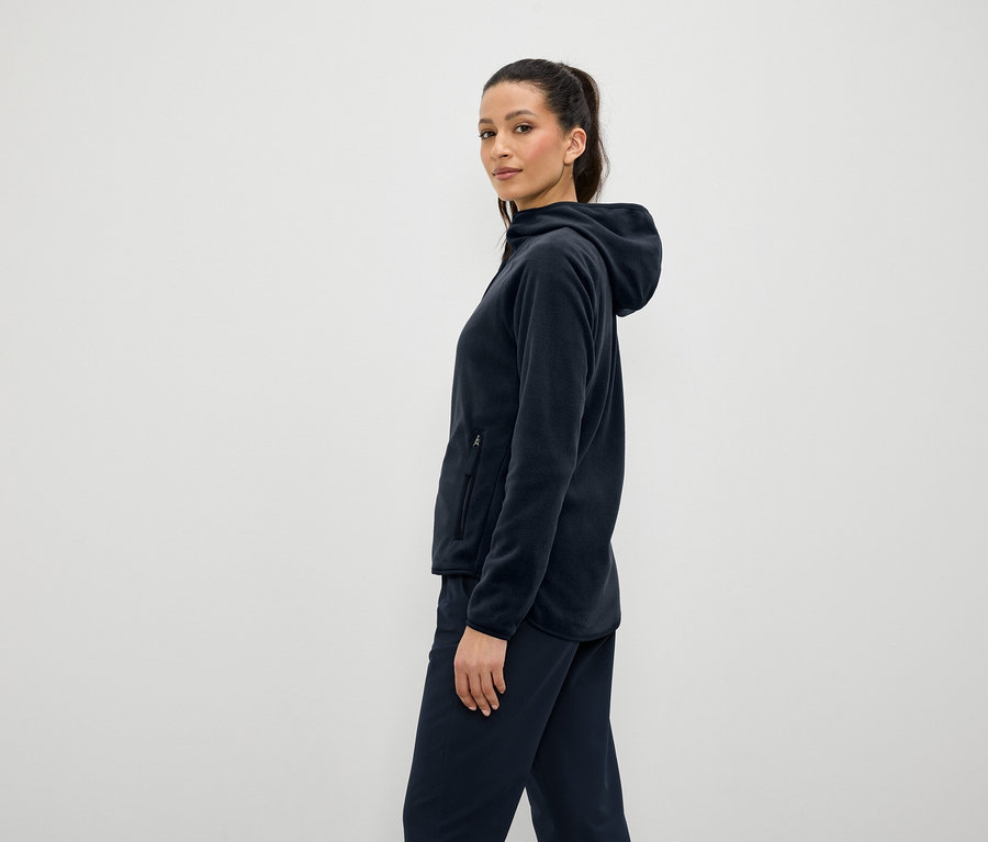 Nő sötétkék polár kapucnis pulóvert és nadrágot visel, oldalra állva.