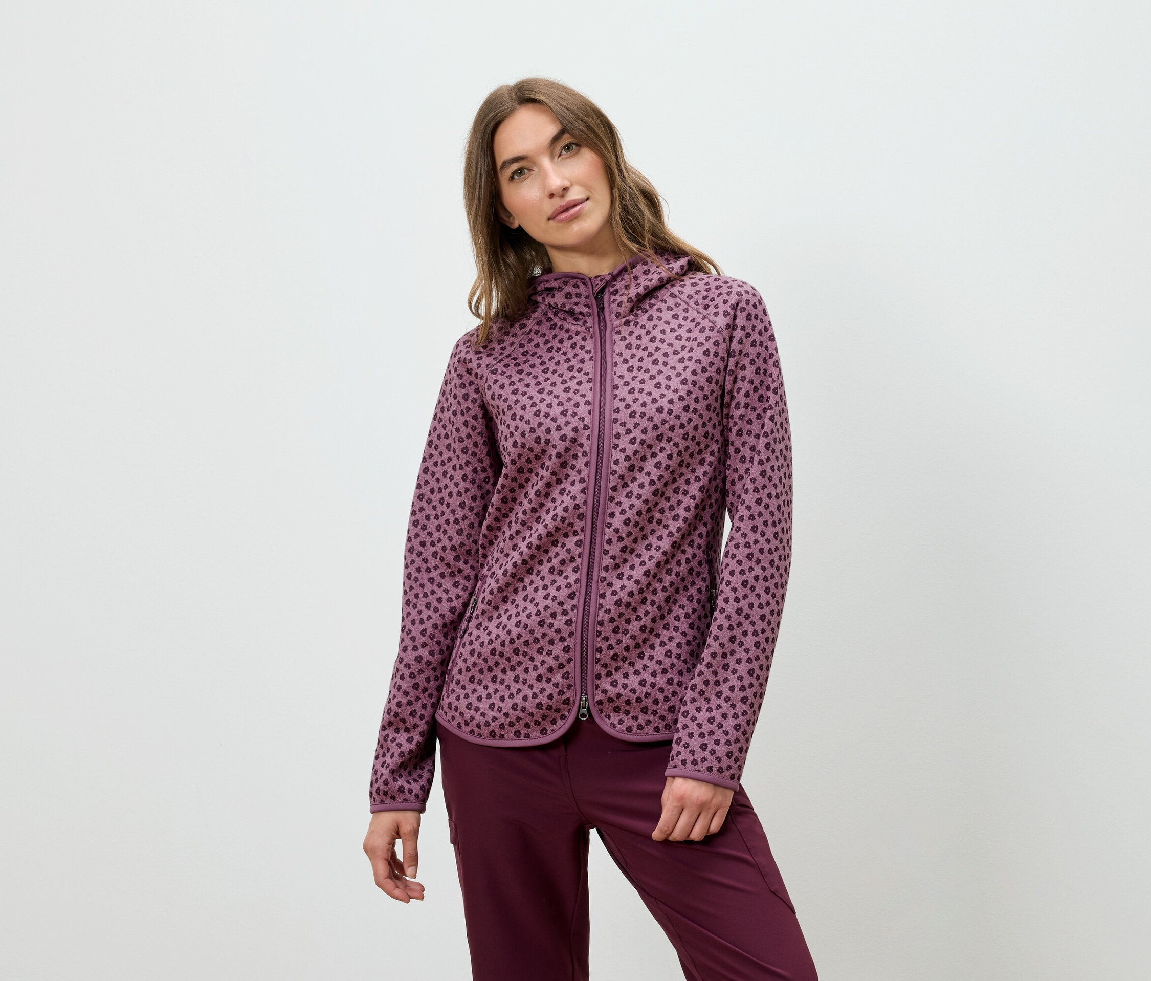 Egy nő bordó színű kapucnis pulóverben és nadrágban pózol.