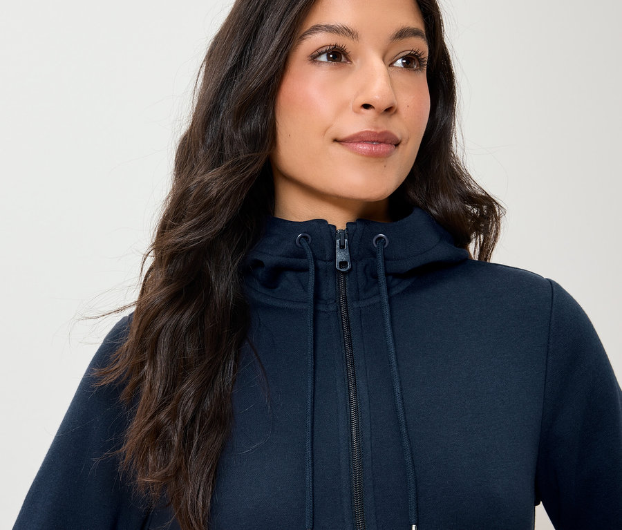 Egy nő tengerészkék, cipzáros kapucnis pulóvert visel.