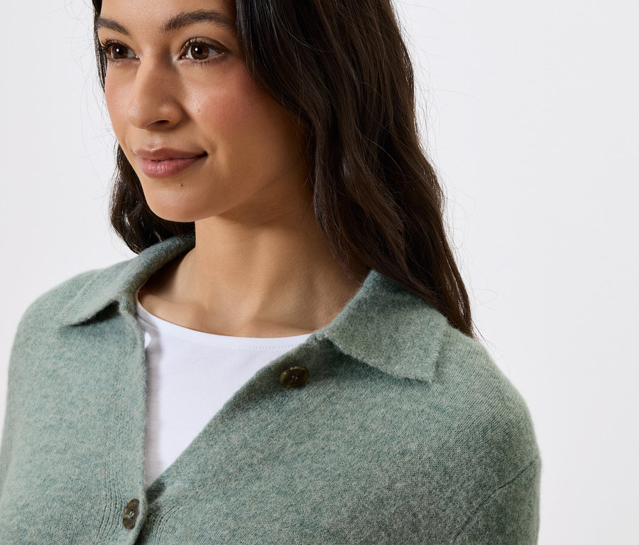 Portré egy sötét hajú nőről, aki zöld, galléros, gombos pulóvert visel.