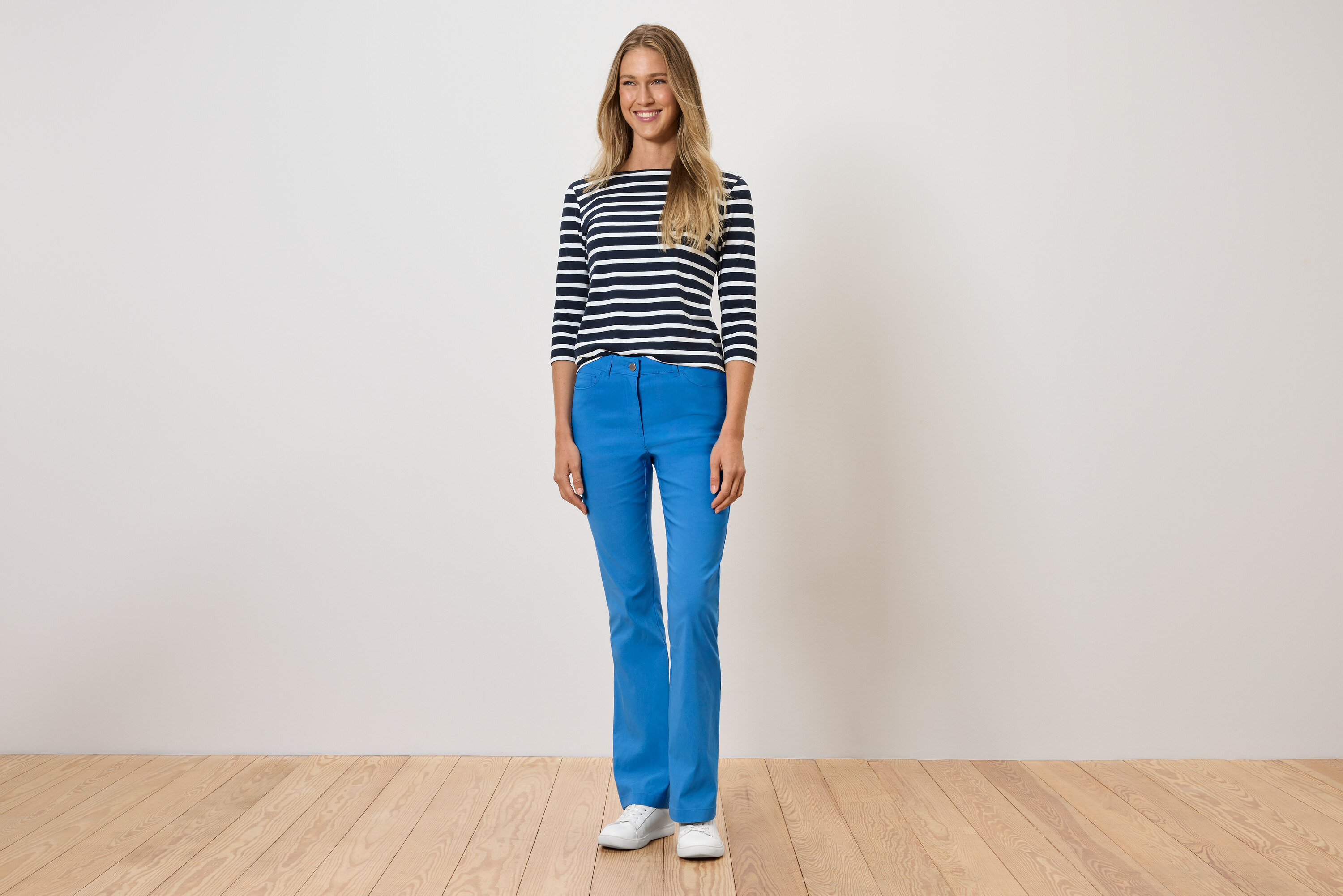 Egy nő áll kék nadrágban, csíkos pólóban és fehér cipőben.