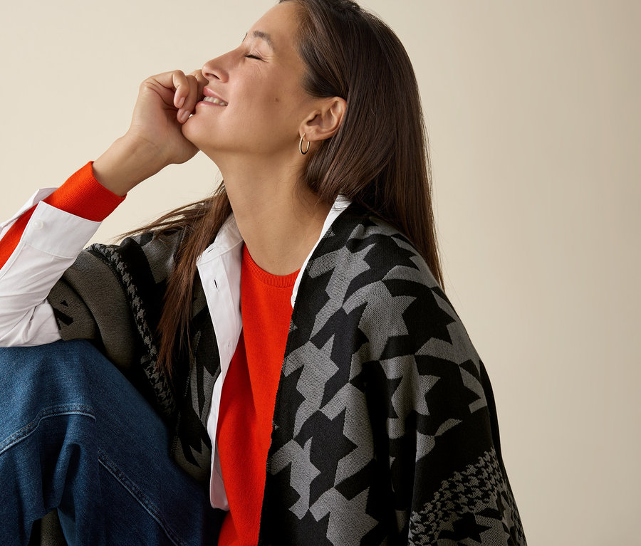 Egy nő ül, és narancssárga, finom kötésű merinó pulóvert visel.