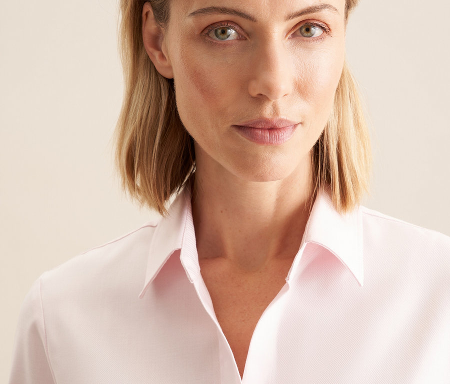Portré egy szőke hajú nőről, aki rózsaszínű Seidensticker twill blúzt visel.