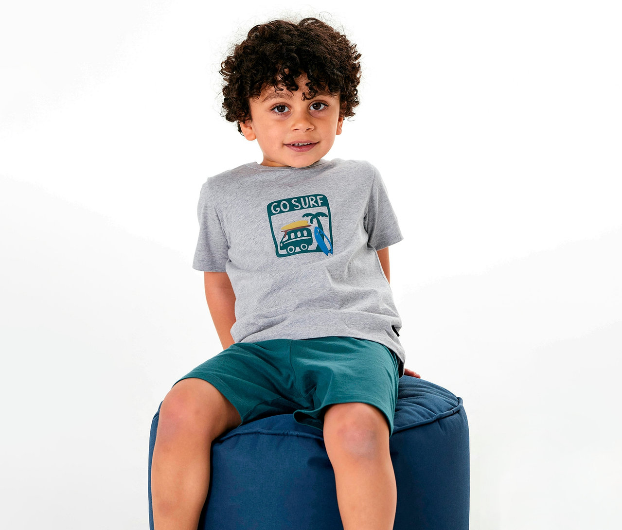 Fiú ül a puffon, SCHIESSER rövidnadrágos gyerekpizsamában.