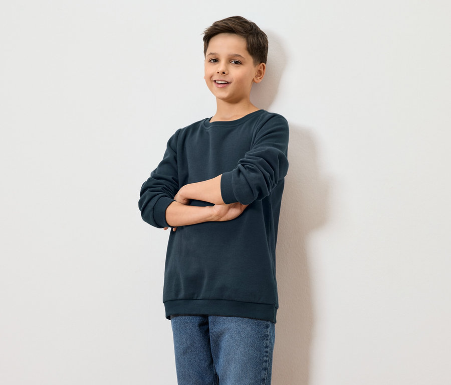 Egy fiú áll keresztbe tett karokkal egy fehér fal előtt.