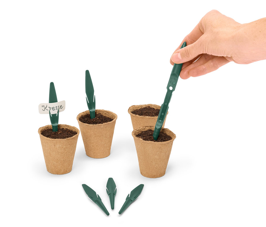 Egy kéz zöld vetőmagrudat helyez egy barna virágcserépbe, amelyet más cserepek és vetőmagrudak vesznek körül.