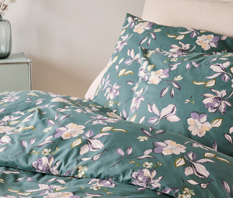 Közelkép egy virágmintás ágyneműről zöld, lila és fehér színekben.