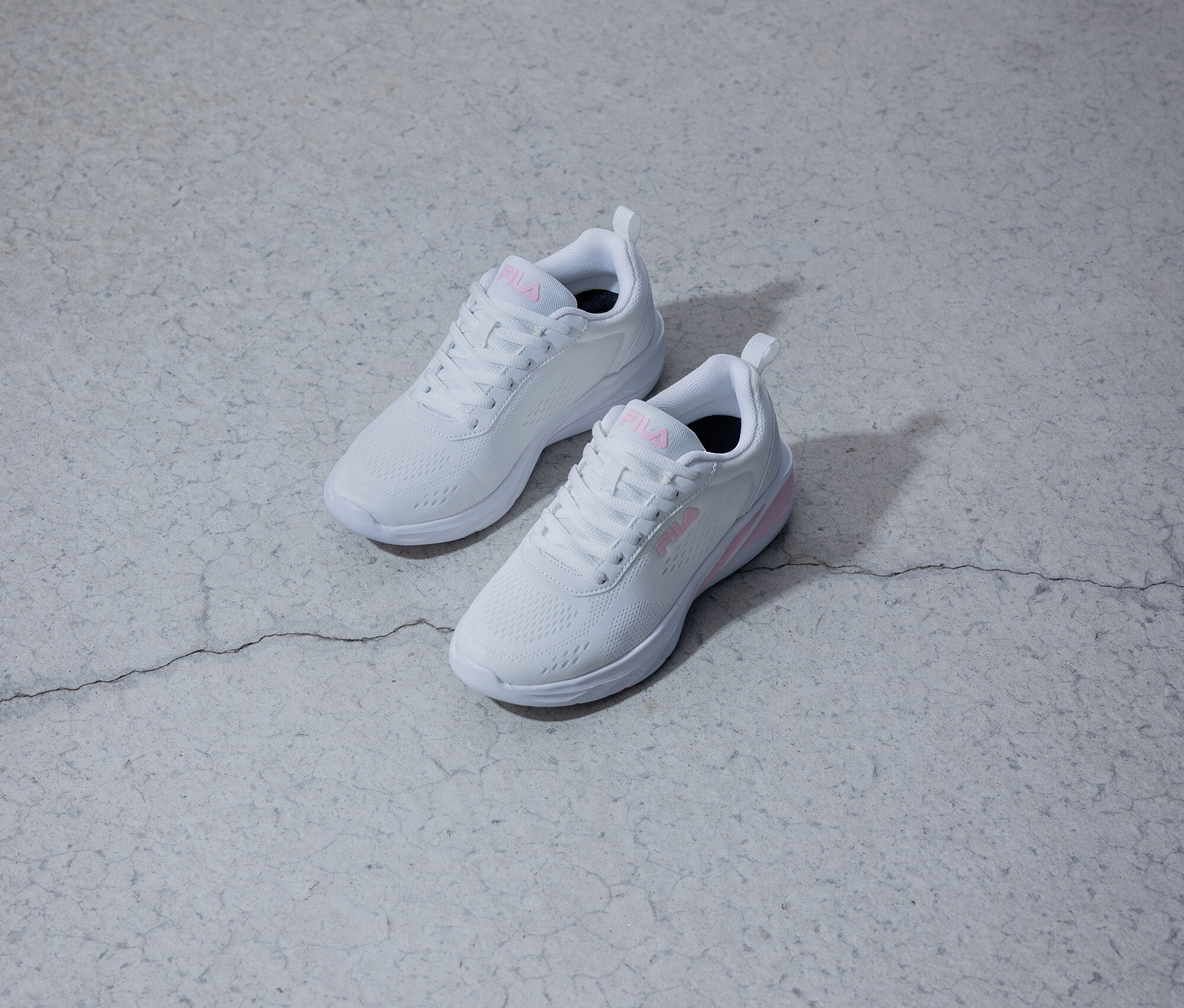Két fehér Fila cipő rózsaszín logóval fekszik egy szürke háttéren.