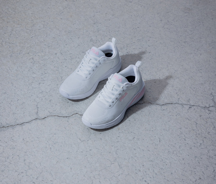 Két fehér Fila cipő rózsaszín logóval fekszik egy szürke háttéren.