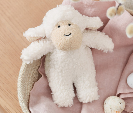 Egy plüssbárány, hanggal, barkás ágakkal és festett tojásokkal teli kosárban fekszik.