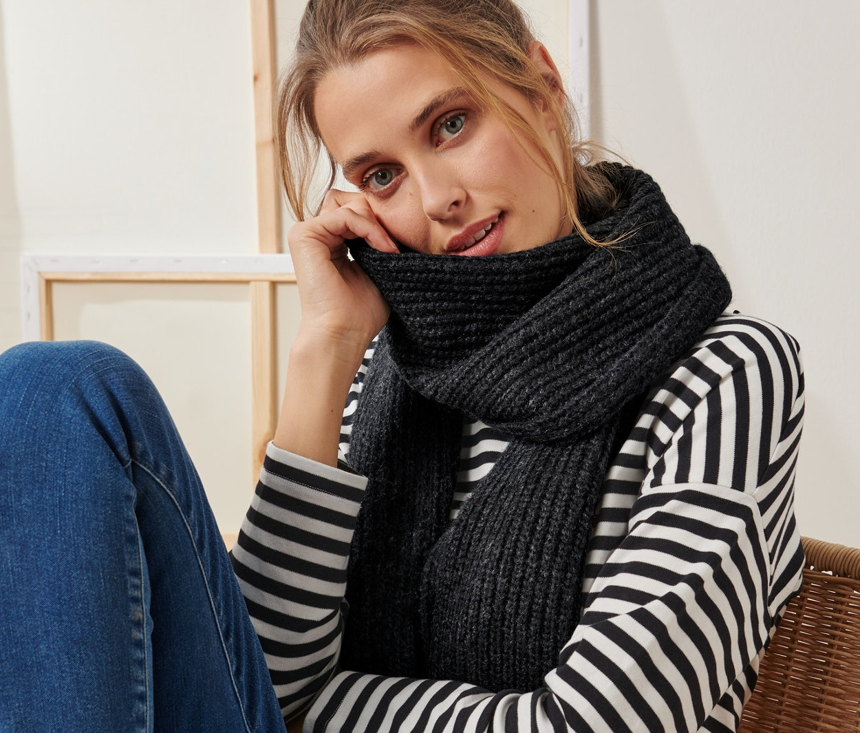 Nő ül egy széken, és antracit színű kötött sálat visel.