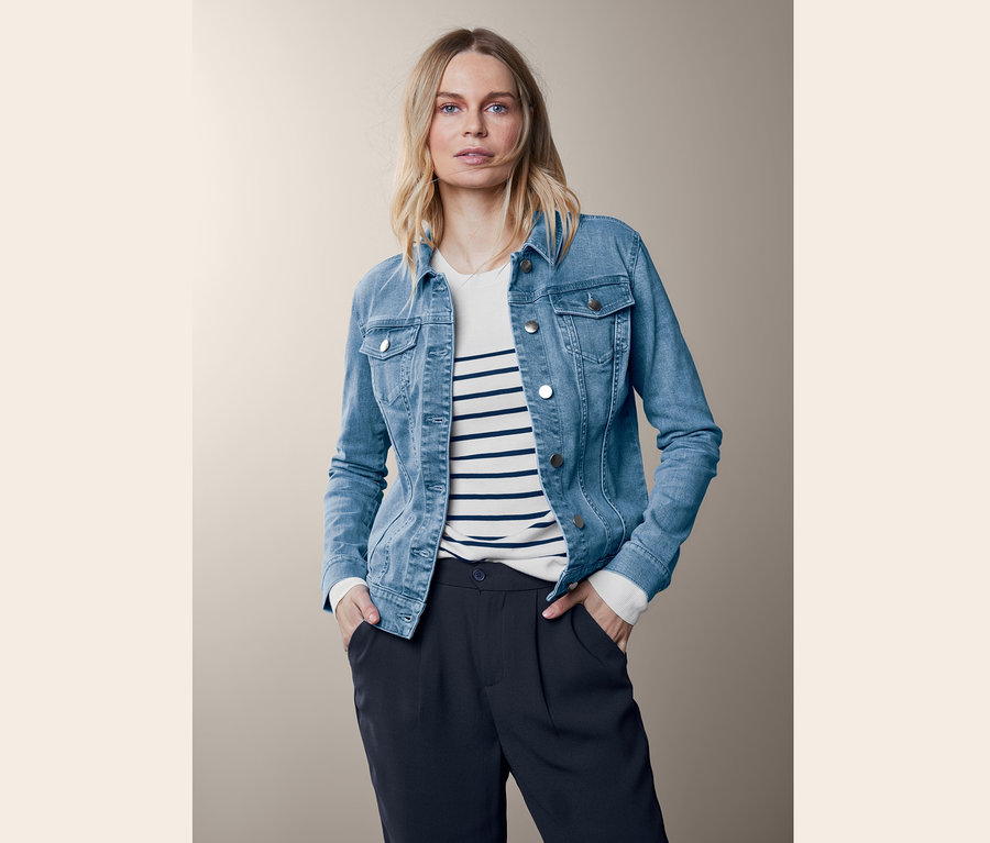 Egy szőke nő pózol kék farmerdzsekiben.