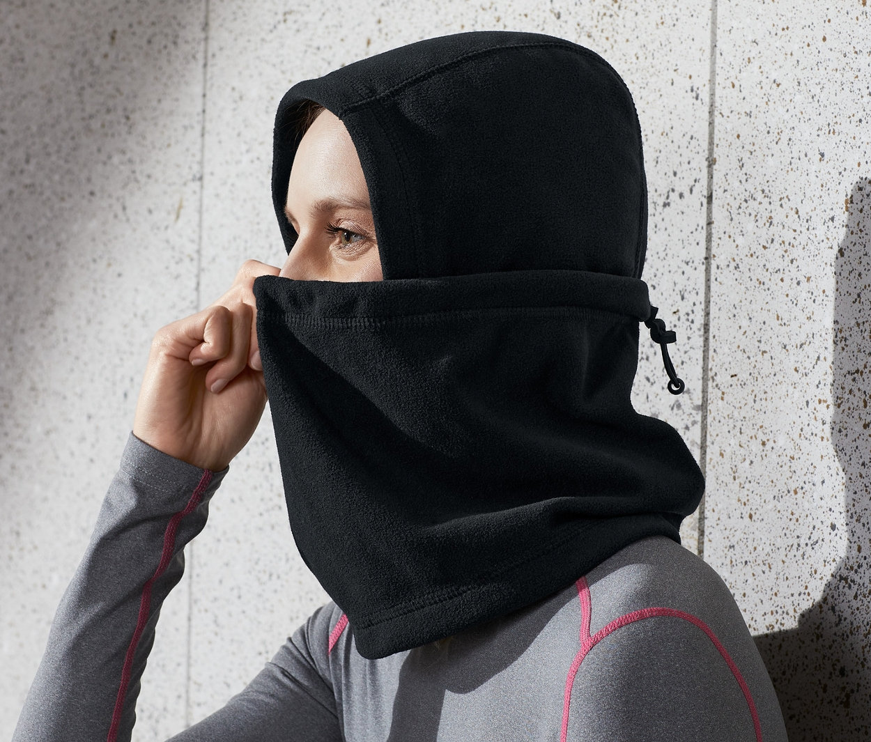 Nő igazítja a fekete mikropolár kámzsát a fején.