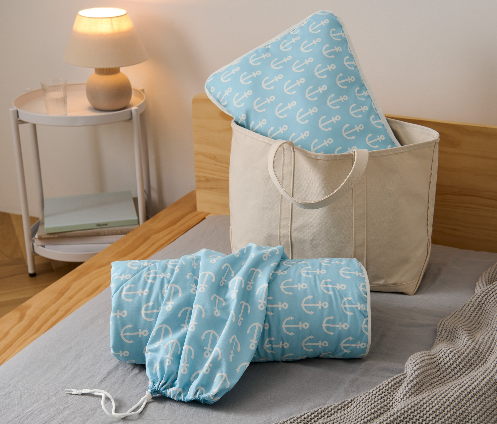 Horgony mintás ágyneműgarnitúra utazáshoz egy bézs színű táskában, valamint feltekerve az ágyon.