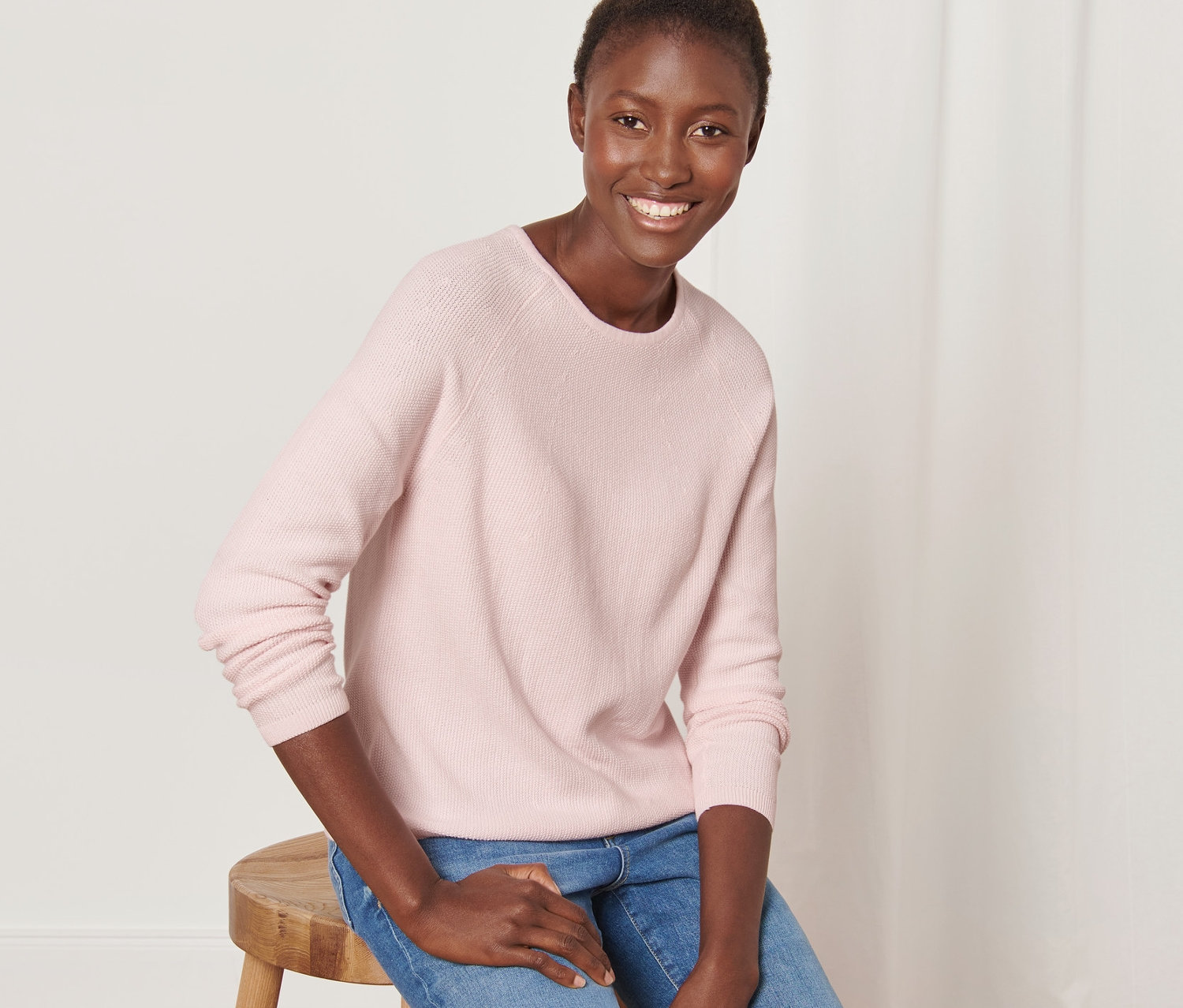 Nő ül egy széken, rózsaszín kötött pulóvert visel.
