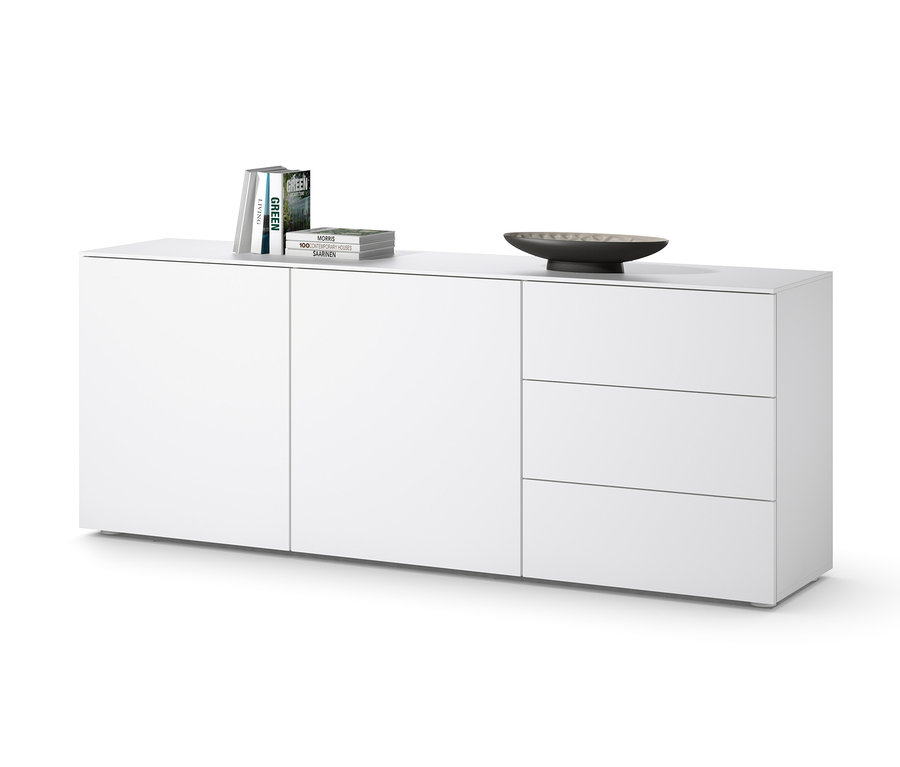 Fehér komód három fiókkal és ajtókkal, tetején könyvekkel és egy tál.