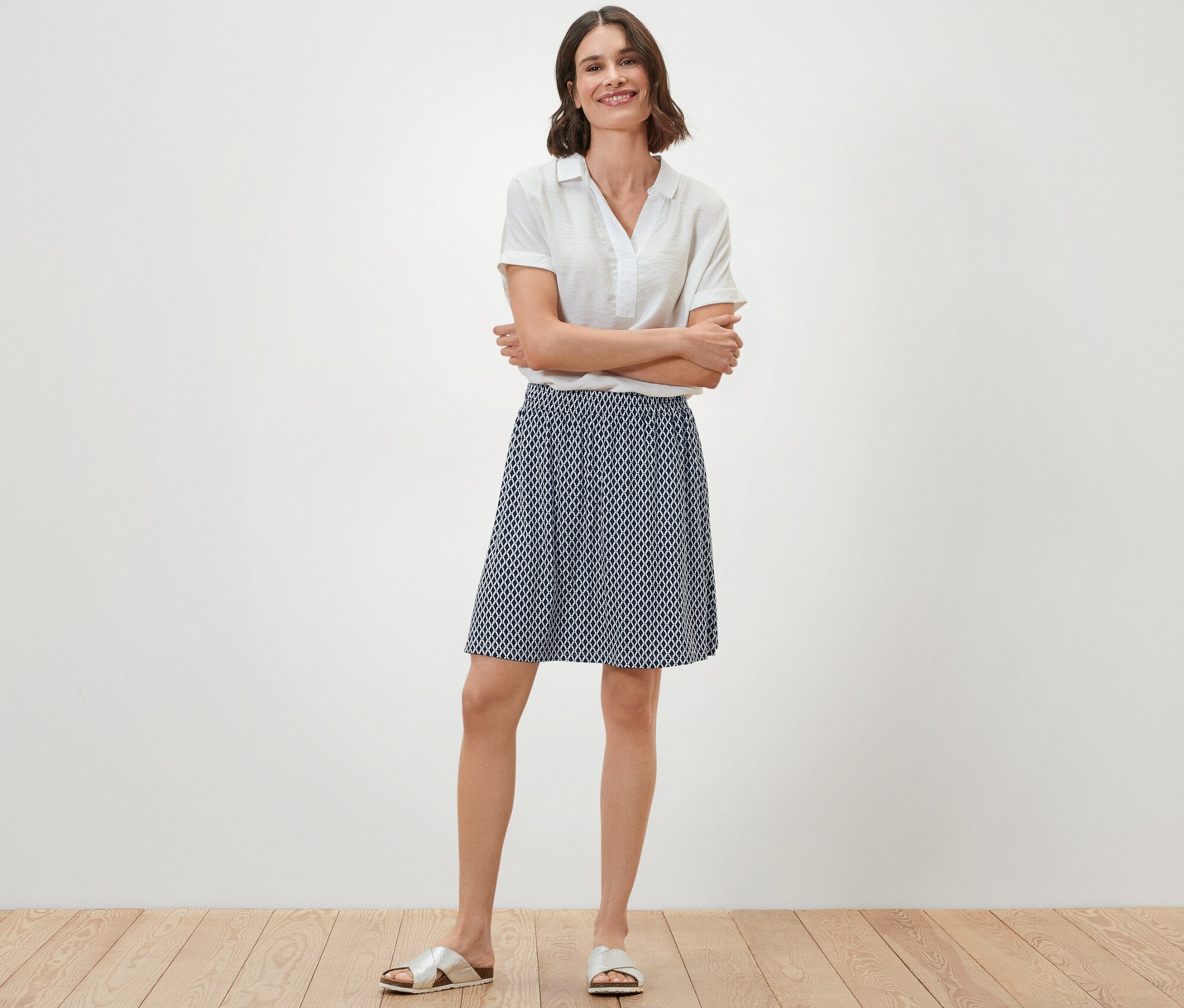 Egy nő áll összekulcsolt karokkal, és egy sötétkék mintás női jersey szoknyát visel.