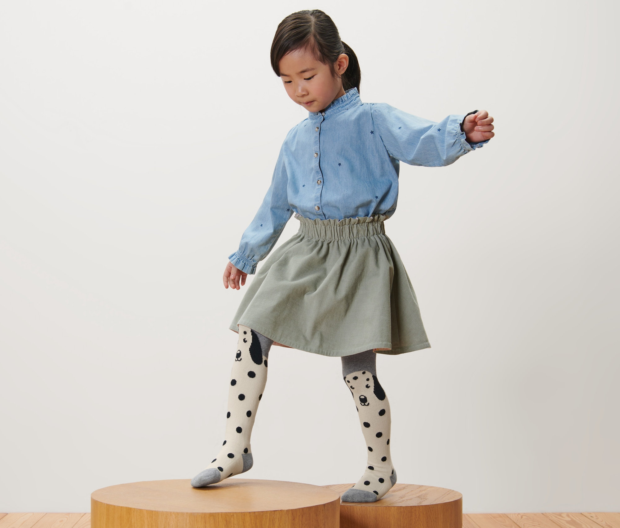 Lány áll egy faemelvényen, rózsaszín, szürke és málnaszínű 3 gyermek harisnyanadrágot visel.