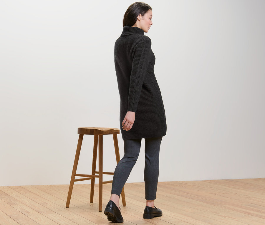 Hátulról látható nő hosszú, fonott mintás, fekete kötött pulóvert visel.