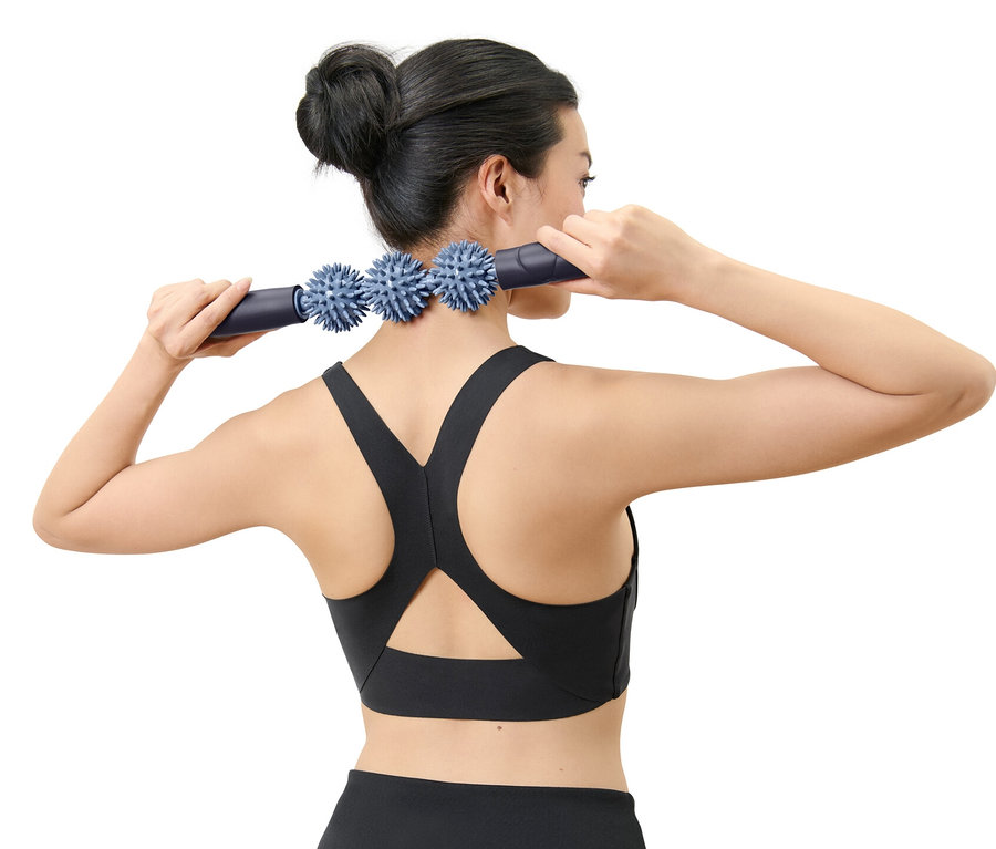 Nő masszázsrúddal masszírozza a nyakát.