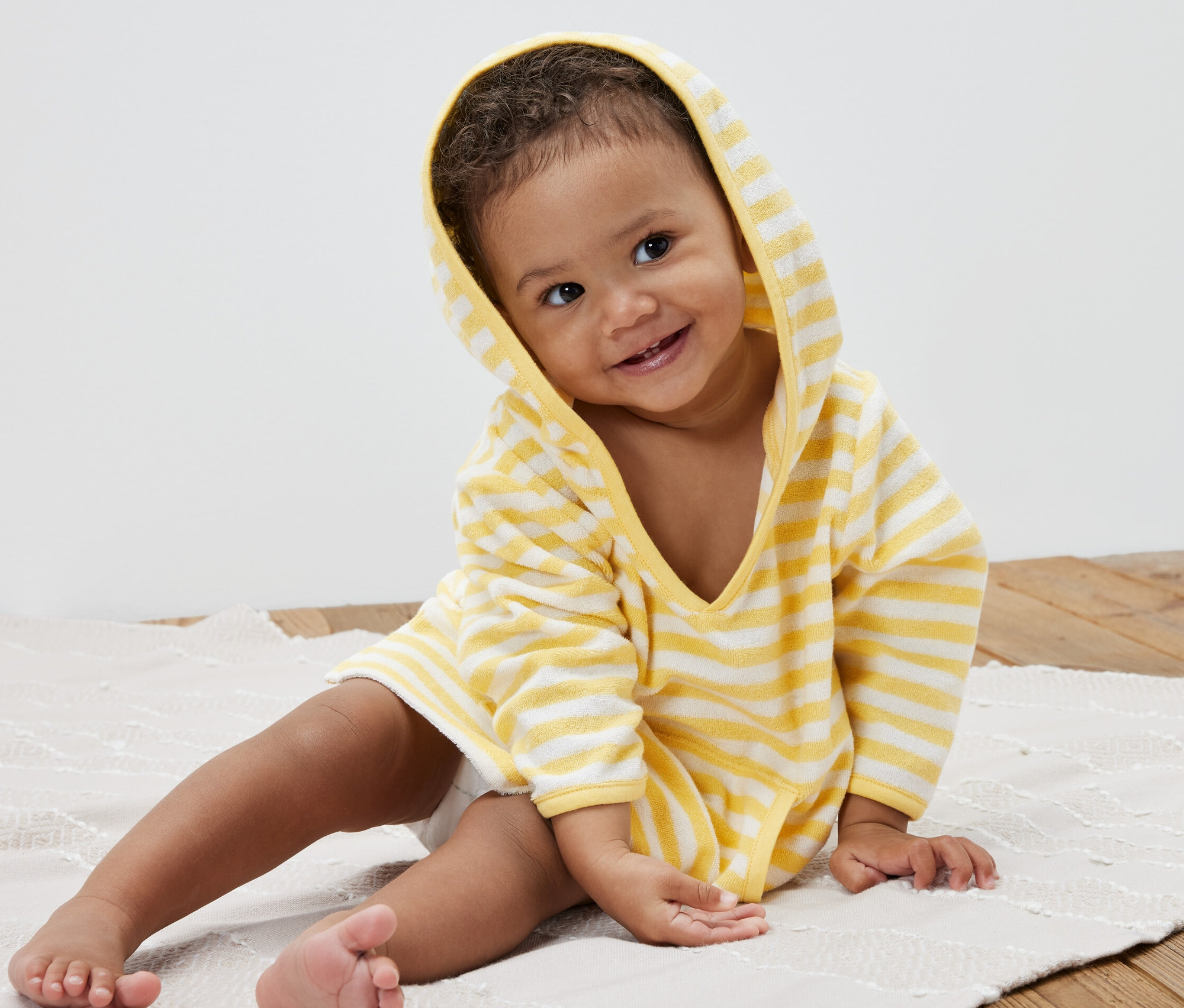 Egy mosolygó gyermek ül egy alátéten, és egy csíkos gyerek frottírponcsót visel.