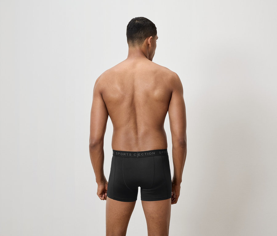 A fényképezőgépnek háttal álló férfi fekete boxeralsót visel.