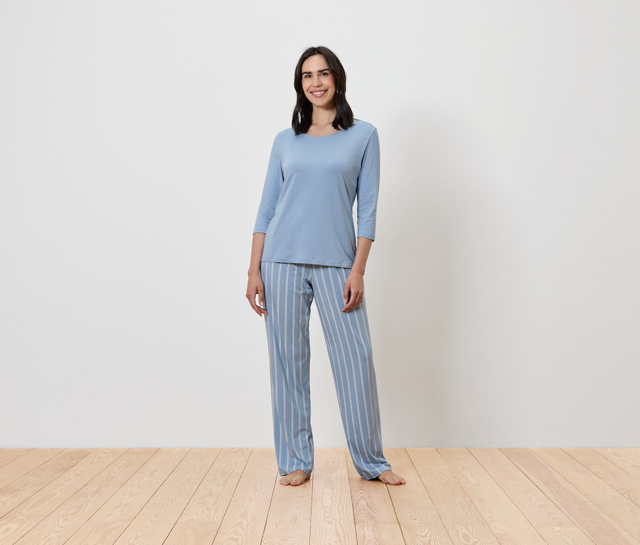 Egy nő áll, kék, csíkos pizsamát visel.
