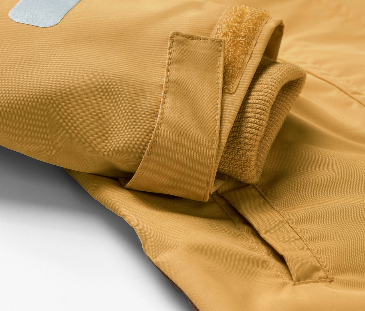 Egy eső elleni kezeslábas részlete zsebbel és fényvisszaverő elemmel.