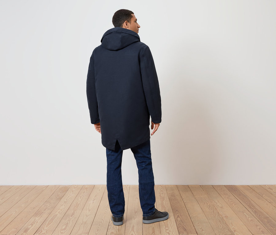Hátulról látható férfi sötétkék kapucnis kabátban, farmerben és cipőben.