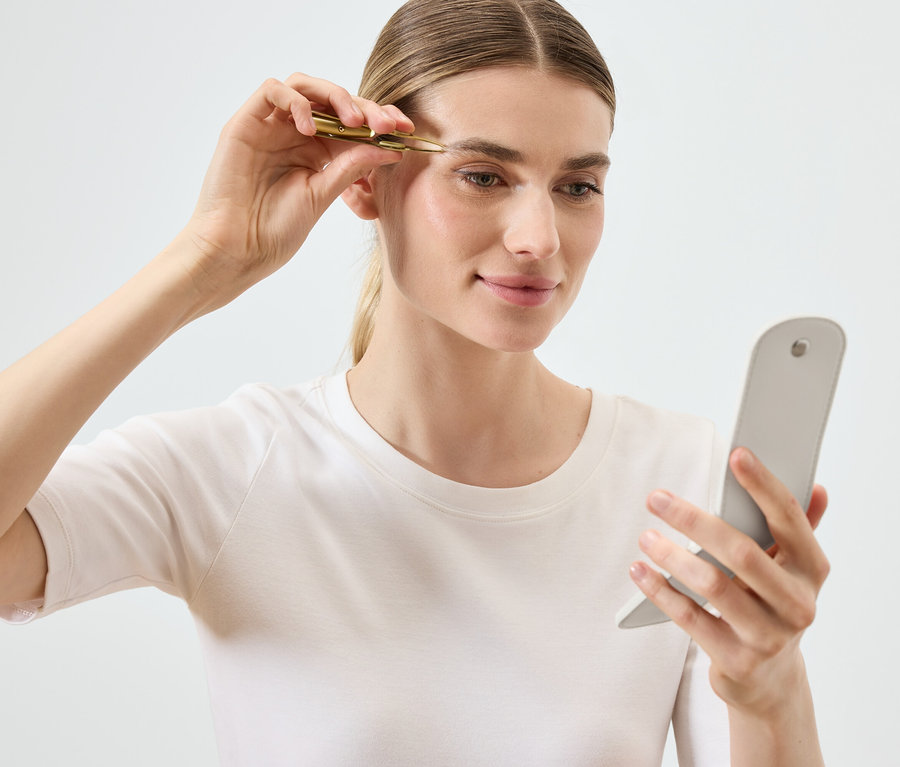 Nő szedi a szemöldökét csipesszel, miközben tükörbe néz.