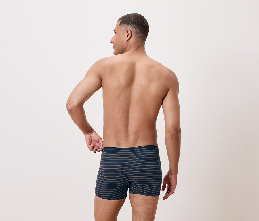 Férfi felsőtest nélkül, hátulról pózol, csíkos boxeralsót visel.